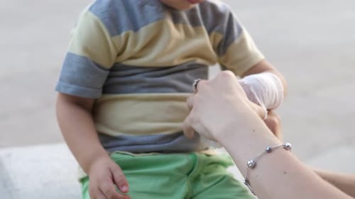 Young Mother Comforting Her Little Son and Giving Him Bandage in a Wounded Hand After Getting Hurt