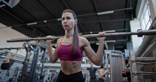 Young Beautiful Woman in Sportswear Doing Workout and Squat Exercises for Legs with Barbell in the