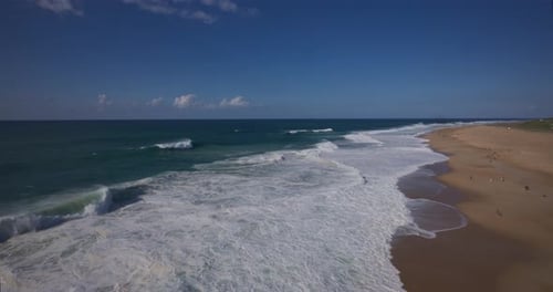 Panoramic Aerial View of Majestic Ocean Waves Crashing on a Sandy Beach Under a Clear Blue Sky