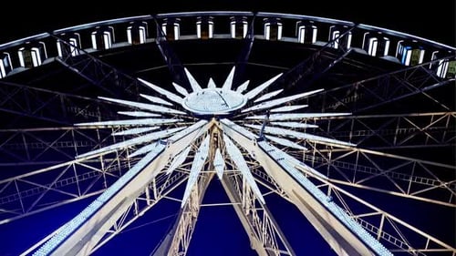 Rotating Illuminated Ferris Wheel From Below with Passenger Gondolas Suspended on the Rim Against a