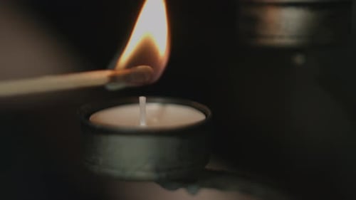 Close up of a tealight in a silver candleholder being lit by a flaring match stick with a dark backg
