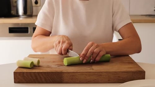 Woman Cutting Leeks on Wooden Board in Kitchen