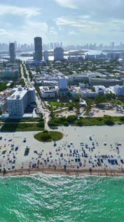 A drone flies sideways over the Atlantic Ocean in portrait mode, capturing ocean waves, beachgoers,