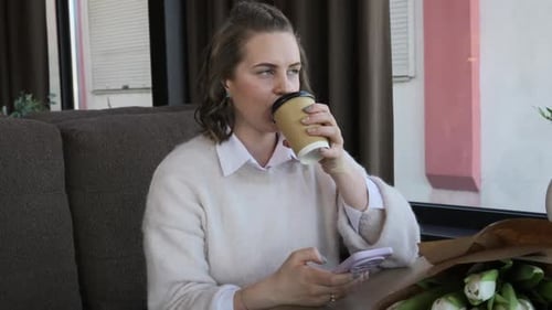 Young Woman Drinking Coffee and Using Smartphone in a Cozy Cafe