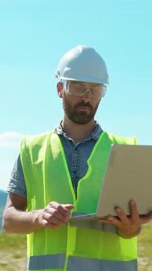 A Construction Worker Utilizing a Laptop to Perform Tasks While on the Job Site Outdoors