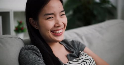 A young woman sits smiling and laughing while thinks of something funny.