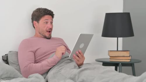 Man Using Tablet in Bed with Positive Reaction