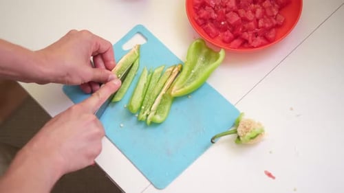 Male Hands Cutting and Slicing Green Bell Pepper with Knife on Cutting Board Cooking at Home