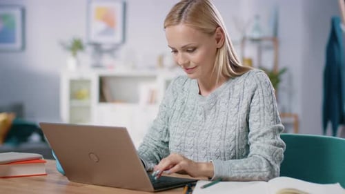 Beautiful Blonde Woman Works on a Laptop while Sitting at Her Desk in the Living Room. Female Profe
