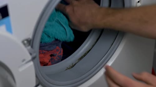 Close-up slow motion hands placing cotton towels into front loader washing machine cleaning detergen