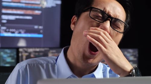 Close Up Of Programmer Yawning And Sleeping While Writing Code By A Laptop Using Multiple Monitors