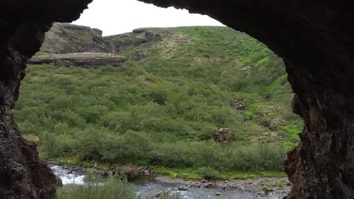 Wild nature with bushes and mountain, flying through cave towards river