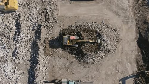 Top down static aerial footage of a backhoe moving rocks on a construction site.