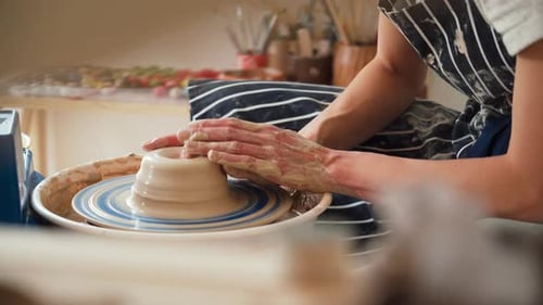 Une potière travaille sur un tour de potier et fabrique un pot en céramique en argile dans un atelier de poterie.