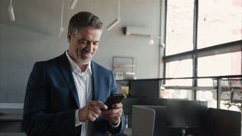 Happy Middle Aged Business Man Wearing Suit Using Cell Phone in Office