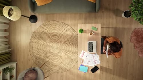 Top View Capturing a Man Having a Videocall on a Laptop in His Home Office Discussing Graphs and