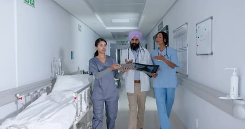 Diverse doctors and nurse using tablet and walking through corridor at hospital, in slow motion