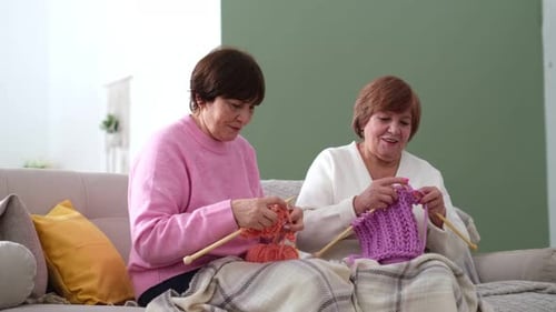 Two Older Women Knitting with Natural Wooden Needles and Environmentally Friendly Pink Wool