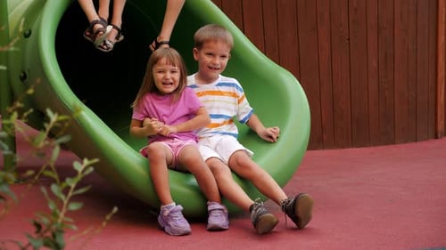 Closeup of Children Sitting on a Plastic Slide on the Playground and Laughing