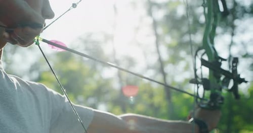 Slow motion close up of young man with professional equipment is practising archery with a bow in