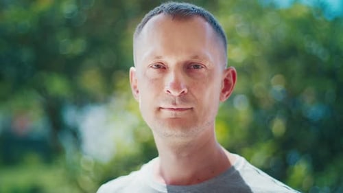 Portrait of the caucasian young adult man looking into the camera over the green garden background