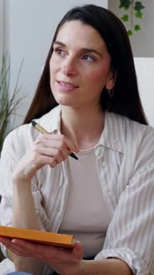 Mid Adult Woman Taking Notes and Thinking in Armchair