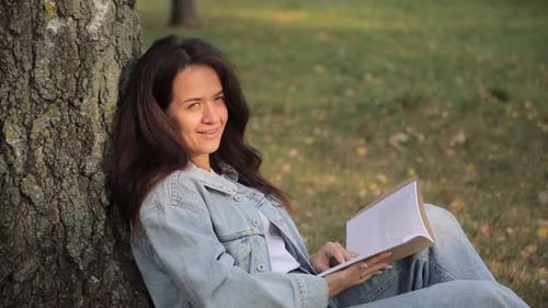 A Woman Reading a Captivating Book Under a Tree in a Serene Park Surrounded By Nature