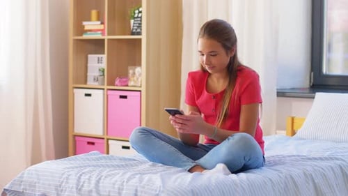 Teenage Girl Using Smartphone Relaxing on Bed at Home