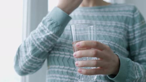 Close Up Glass of Water in Hand of Woman Who Washes Down Antiviral Pill