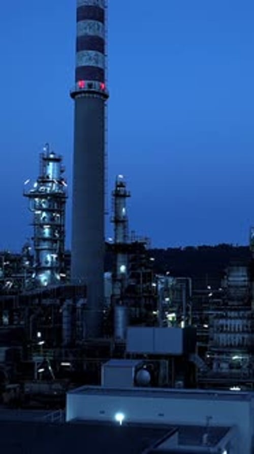 Un paysage industriel au crépuscule avec une cheminée de fumée proéminente et des raffineries à proximité