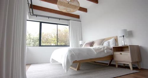 Interior of domestic bedroom with double bed and window overlooking garden, copy space, slow motion