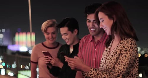 Group of friends on smartphones outdoors in city at night