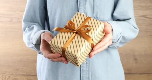 Man with beautiful gift box on wooden background, closeup