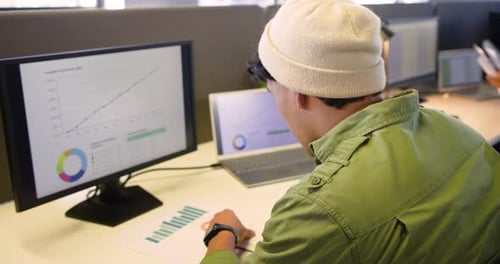 Data analyst spotting growth charts and studying bar chart at desk while colleagues typing pointing