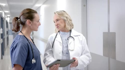 Caucasian female doctors in discussion using tablet in hospital corridor, slow motion