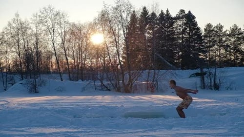 Man Jumping Into Ice Hole at Sunrise in Winter