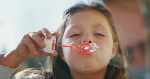 Gros plan authentique d'une petite fille soufflant des bulles de savon dans un parc printanier par une journée ensoleillée.