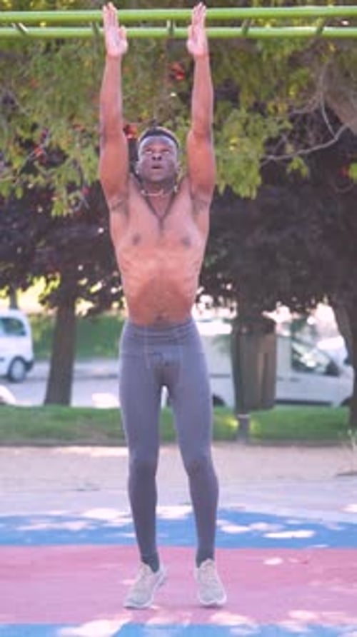 Young fit shirtless black man doing burpees outdoors on sunny summer day.