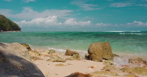 Tropical white sand beach sea water foams and spalshes on rocks, close-up. Blue turquoise ocean rush