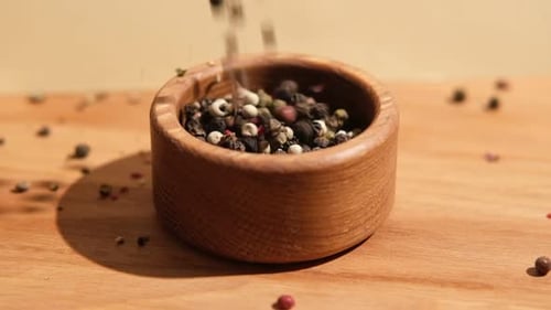 Peppercorns Being Poured Into a Wooden Bowl