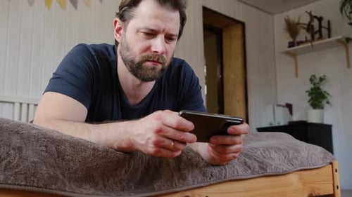 Man Lying on Bed Playing on Smartphone