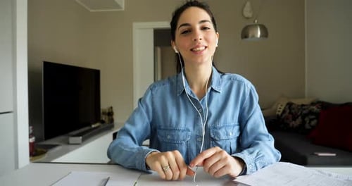 An Young Woman with Earphones is Making a Video Conference Call with a Laptop to Colleagues while