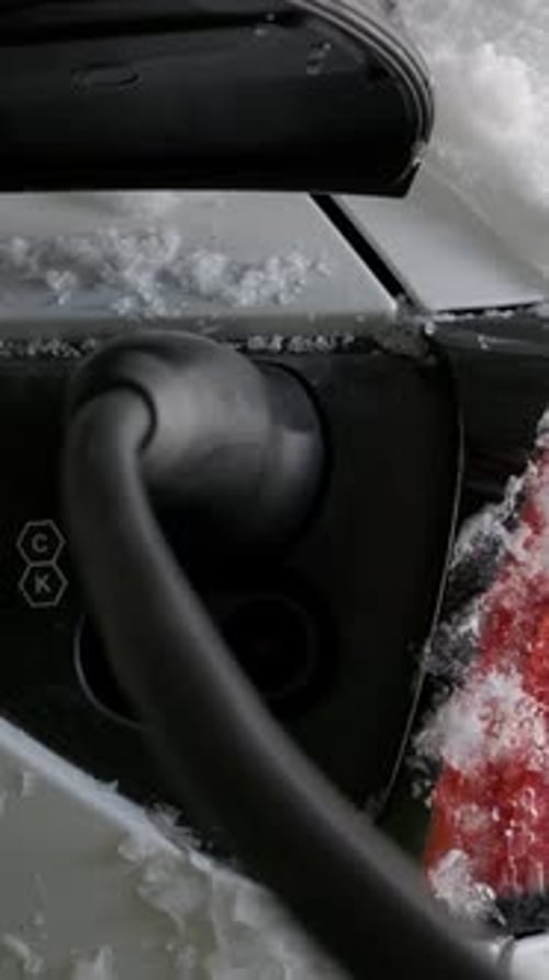 Ladeanschluss für Elektroautos mit Kabel, bedeckt mit winterlichem Schnee und Eis