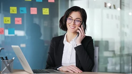 Confident businesswoman having a phone conversation while sitting at a workplace in the office.