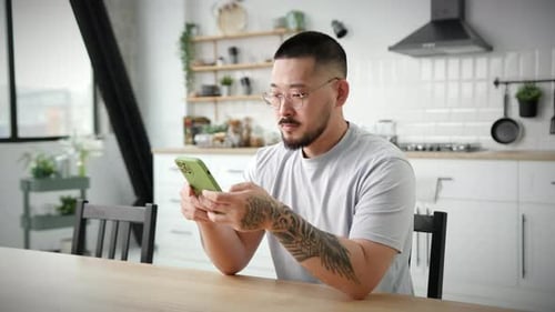 Man Uses Smartphone at Kitchen Table