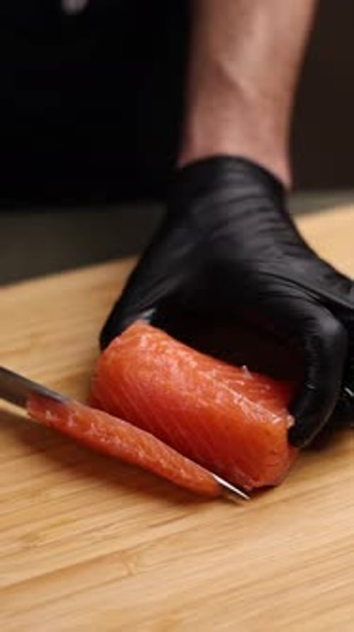 Close-up of a chef slicing fresh salmon on a wooden cutting board.