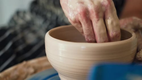 A female potter works on a potter's wheel, making a ceramic pot from clay in a pottery workshop.