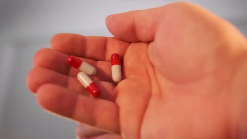Close-up holding red white capsules pills in palm of hand. Vitamins and medicines.