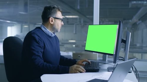 Man Working at Desk with Green Screen Computer