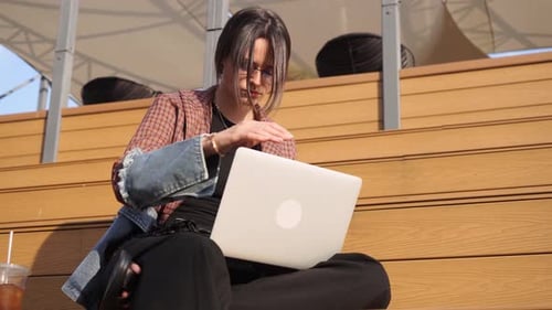 Young attractive brunette student works at her laptop on campus. Hipster outfit. close-up